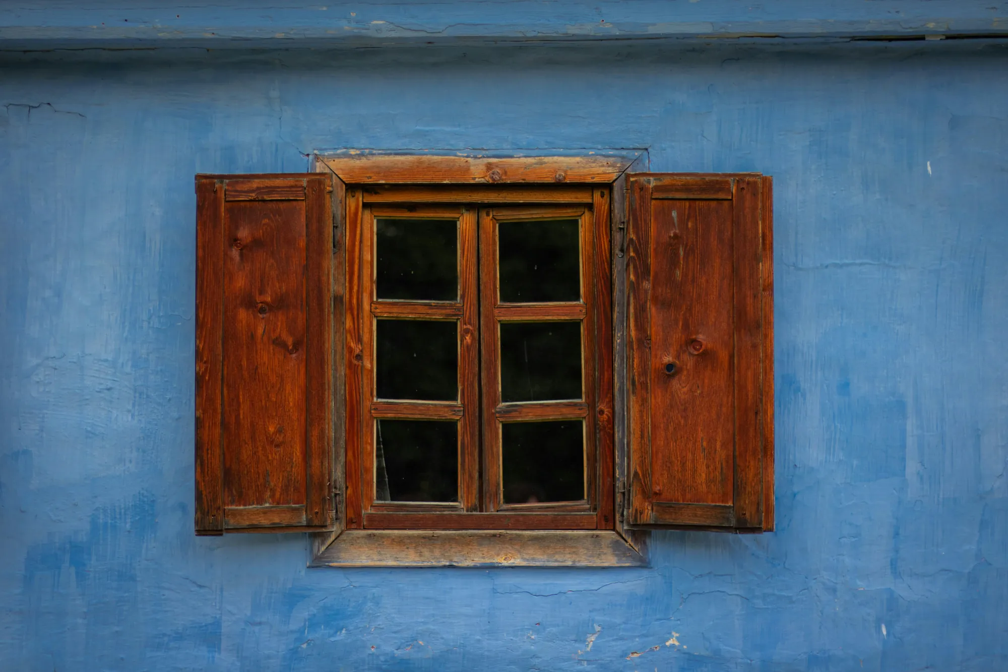 A wooden window with open wooden shutters set into a blue plastered wall