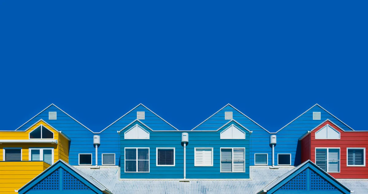 A row of freshly painted houses in yellow, blue and red under a clear blue sky